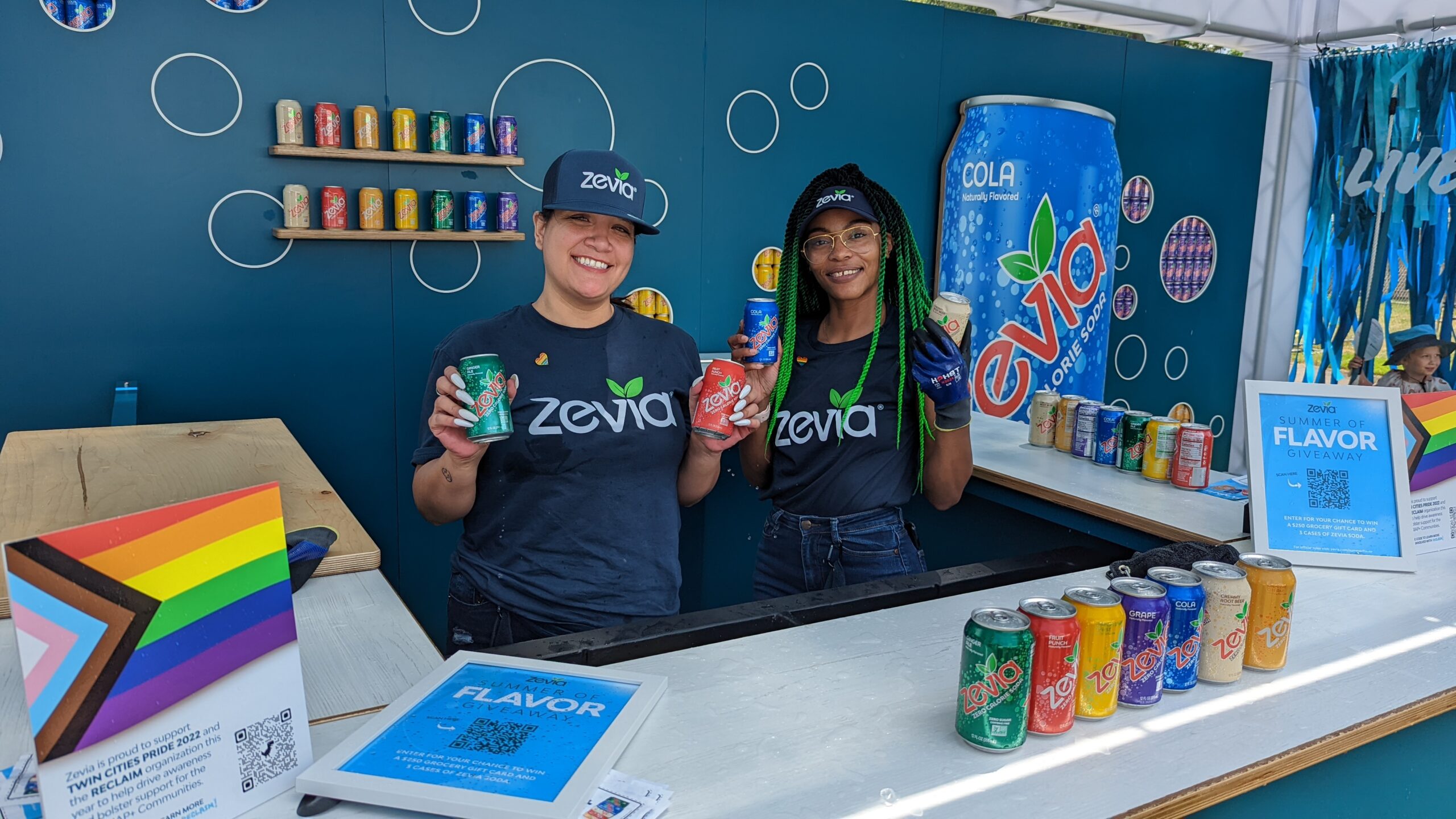 Two Evolve Activation Brand Ambassadors Sampling Zevia Beverages at Pride in Minneapolis, Refreshing Product Engagement at a High-energy Experiential Event.